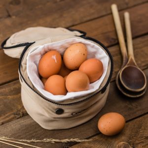 Jajka umieszczone w materiałowym pojemniku. Obok znajdują się drewniane chochle.